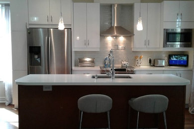 Mid-sized transitional galley brown floor and dark wood floor open concept kitchen photo in Toronto with an undermount sink, flat-panel cabinets, white cabinets, solid surface countertops, gray backsplash, subway tile backsplash, stainless steel appliances and an island