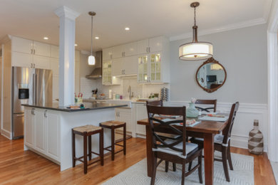 Mid-sized transitional l-shaped medium tone wood floor and brown floor eat-in kitchen photo in New York with a farmhouse sink, raised-panel cabinets, white cabinets, solid surface countertops, white backsplash, subway tile backsplash, stainless steel appliances, an island and white countertops