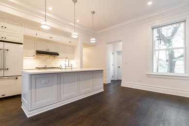 Inspiration for a mid-sized transitional single-wall dark wood floor and brown floor eat-in kitchen remodel in New York with an undermount sink, shaker cabinets, white cabinets, solid surface countertops, white backsplash, marble backsplash, white appliances and an island