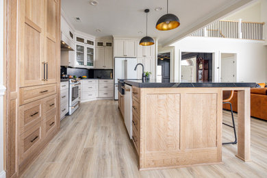 Open concept kitchen - mid-sized transitional l-shaped open concept kitchen idea in Charlotte with a farmhouse sink, recessed-panel cabinets, beige cabinets, quartz countertops, black backsplash, quartz backsplash, white appliances, an island and black countertops