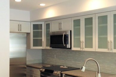 Small trendy u-shaped porcelain tile and gray floor kitchen photo in Hawaii with an undermount sink, glass-front cabinets, white cabinets, quartzite countertops, white backsplash, glass sheet backsplash, stainless steel appliances and a peninsula