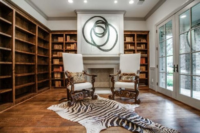 Inspiration for a mid-sized transitional home office in Dallas with a library, white walls, dark hardwood floors, a standard fireplace, a stone fireplace surround and brown floor.