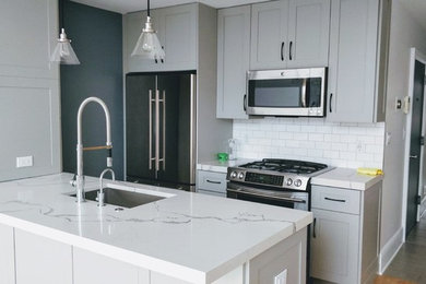 Small minimalist galley light wood floor and brown floor eat-in kitchen photo in New York with an undermount sink, shaker cabinets, gray cabinets, quartz countertops, stainless steel appliances, white backsplash, subway tile backsplash, an island and white countertops