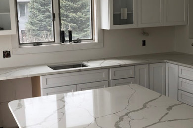 Large trendy l-shaped medium tone wood floor and brown floor eat-in kitchen photo in Chicago with a drop-in sink, shaker cabinets, white cabinets, quartzite countertops, white backsplash and an island