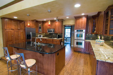 Example of a large transitional u-shaped medium tone wood floor and brown floor eat-in kitchen design in Chicago with beaded inset cabinets, medium tone wood cabinets, granite countertops, an island, multicolored countertops, a double-bowl sink, black backsplash, ceramic backsplash and stainless steel appliances