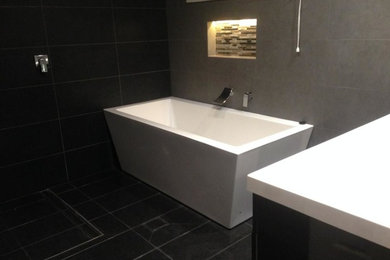 This is an example of a modern bathroom in Sydney with a console sink, a freestanding tub, an open shower, black tile, stone slab, grey walls and porcelain floors.