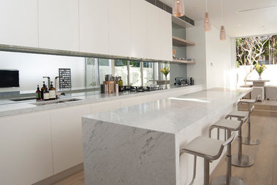 This is an example of a mid-sized contemporary galley eat-in kitchen in Sydney with marble benchtops, glass sheet splashback and light hardwood floors.