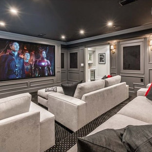 This is an example of a large traditional enclosed home cinema in Los Angeles with grey walls, carpet, a projector screen and black floors.