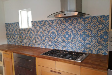 Example of a mid-sized eclectic u-shaped open concept kitchen design in Austin with flat-panel cabinets, medium tone wood cabinets, wood countertops, blue backsplash, cement tile backsplash, stainless steel appliances and an island