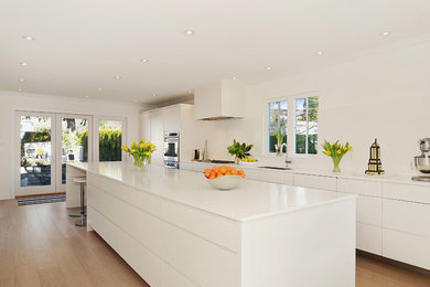Inspiration for a large modern single-wall medium tone wood floor open concept kitchen remodel in Vancouver with an undermount sink, white cabinets, white backsplash, stainless steel appliances and an island