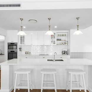 Idées déco pour une grande arrière-cuisine parallèle classique avec un évier encastré, un placard à porte shaker, des portes de placard blanches, un plan de travail en quartz modifié, une crédence blanche, une crédence en carrelage métro, un électroménager en acier inoxydable, un sol en linoléum, un îlot central, un sol marron et un plan de travail jaune.