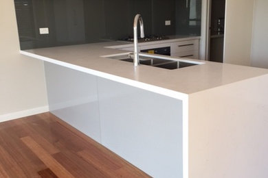 Photo of a mid-sized l-shaped open plan kitchen in Melbourne with an undermount sink, quartz benchtops, glass sheet splashback and with island.