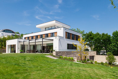 This is an example of an expansive mediterranean three-storey stucco white house exterior in Munich with a flat roof.