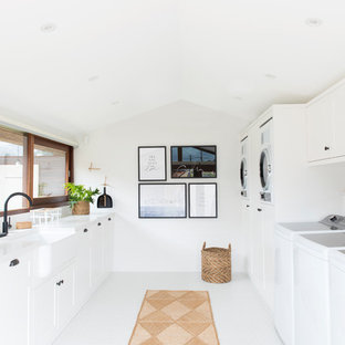 Photo of an expansive contemporary galley separated utility room in Gold Coast - Tweed with a belfast sink, shaker cabinets, white cabinets, engineered stone countertops, white walls, porcelain flooring, white floors and a side by side washer and dryer.