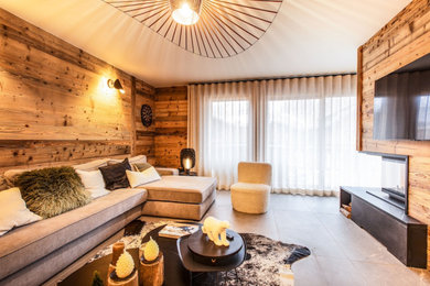 Cette image montre un grand salon gris et noir chalet en bois ouvert avec un sol en carrelage de céramique, une cheminée double-face, un manteau de cheminée en bois, un téléviseur fixé au mur et un sol gris.