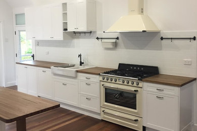 Inspiration for a country galley eat-in kitchen in Brisbane with a farmhouse sink, white cabinets, wood benchtops, white splashback, ceramic splashback, coloured appliances, dark hardwood floors, with island and brown floor.