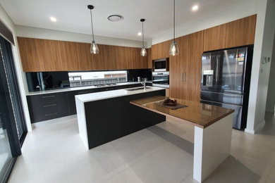 Design ideas for a large contemporary l-shaped eat-in kitchen in Sydney with an undermount sink, flat-panel cabinets, dark wood cabinets, glass benchtops, black splashback, engineered quartz splashback, panelled appliances, porcelain floors, multiple islands, grey floor and white benchtop.