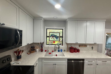 Example of a farmhouse brown floor kitchen design in Austin with shaker cabinets, white cabinets, quartz countertops, stainless steel appliances and an island