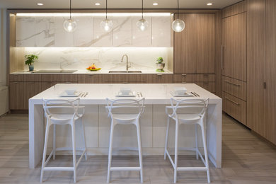 Trendy l-shaped brown floor kitchen photo in New York with an undermount sink, flat-panel cabinets, medium tone wood cabinets, white backsplash, stone slab backsplash, paneled appliances and an island