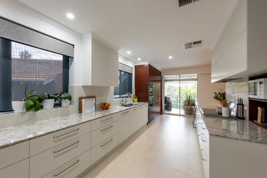 This is an example of a large modern galley kitchen pantry in Perth with an undermount sink, flat-panel cabinets, white cabinets, quartz benchtops, grey splashback, porcelain splashback, black appliances, porcelain floors, no island, white floor and multi-coloured benchtop.