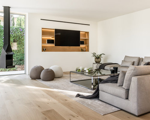 Diseño de sala de estar abierta, actual, con paredes blancas, suelo de madera clara, chimeneas suspendidas, pared multimedia y marco de chimenea de metal