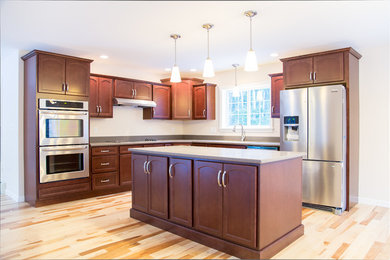 Example of a light wood floor kitchen design in Portland Maine with medium tone wood cabinets, stainless steel appliances and an island