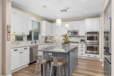 Example of a mid-sized transitional u-shaped vinyl floor and brown floor open concept kitchen design in San Diego with an undermount sink, raised-panel cabinets, white cabinets, quartz countertops, gray backsplash, ceramic backsplash, stainless steel appliances, an island and blue countertops