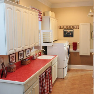 ワシントンD.C.の大きいカントリー風おしゃれな洗濯室 (レイズドパネル扉のキャビネット、白いキャビネット、ベージュの壁、左右配置の洗濯機・乾燥機、ドロップインシンク、ラミネートの床、赤いキッチンカウンター) の写真
