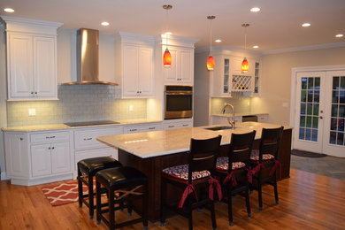 Open concept kitchen - large contemporary single-wall light wood floor open concept kitchen idea in New York with an undermount sink, raised-panel cabinets, white cabinets, granite countertops, white backsplash, ceramic backsplash, stainless steel appliances and an island