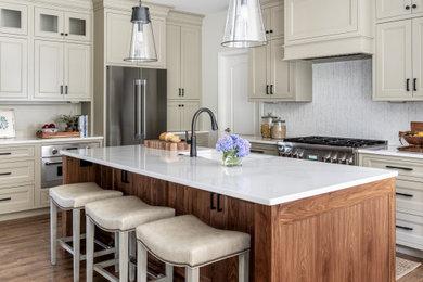 Mid-sized transitional galley medium tone wood floor and brown floor eat-in kitchen photo in Philadelphia with an undermount sink, flat-panel cabinets, beige cabinets, quartz countertops, white backsplash, glass sheet backsplash, stainless steel appliances, an island and white countertops