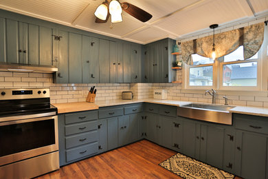 Mid-sized country l-shaped medium tone wood floor and brown floor eat-in kitchen photo in New York with shaker cabinets, blue cabinets, no island, a farmhouse sink, marble countertops, white backsplash, subway tile backsplash, stainless steel appliances and white countertops