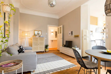 Diseño de sala de estar abierta escandinava de tamaño medio con paredes beige, suelo de madera clara, televisor independiente y ladrillo