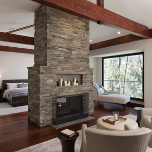 Photo of an expansive modern master bedroom in San Diego with white walls, medium hardwood floors, a two-sided fireplace, a stone fireplace surround and brown floor.