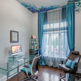 This is an example of a mid-sized contemporary study room with beige walls, dark hardwood floors, a plaster fireplace surround, a freestanding desk, a standard fireplace and brown floor.