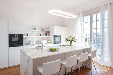 Inspiration for a medium sized contemporary galley enclosed kitchen in Nice with an integrated sink, beaded cabinets, white cabinets, marble worktops, white splashback, marble splashback, black appliances, light hardwood flooring, an island, beige floors and white worktops.