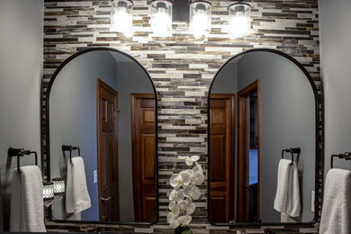 Photo of a small transitional 3/4 bathroom in Cleveland with raised-panel cabinets, brown cabinets, an alcove tub, a shower/bathtub combo, a two-piece toilet, gray tile, mosaic tile, grey walls, vinyl floors, an integrated sink, solid surface benchtops, brown floor, a shower curtain, white benchtops, an enclosed toilet, a double vanity and a built-in vanity.