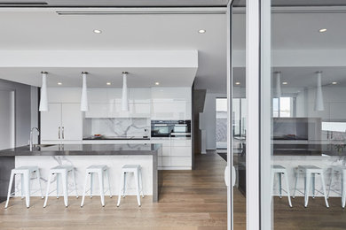 This is an example of a mid-sized contemporary l-shaped eat-in kitchen in Perth with a drop-in sink, shaker cabinets, laminate benchtops, white splashback, marble splashback, stainless steel appliances, medium hardwood floors, with island and brown floor.