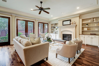 Diseño de sala de estar abierta clásica renovada de tamaño medio con paredes beige, suelo de madera en tonos medios, marco de chimenea de piedra y suelo marrón