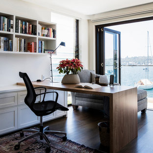 This is an example of a transitional study room in Sydney with beige walls, dark hardwood floors, a built-in desk and brown floor.