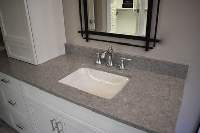 Inspiration for a mid-sized transitional master gray tile and subway tile porcelain tile and white floor bathroom remodel in Charlotte with recessed-panel cabinets, white cabinets, a two-piece toilet, gray walls, an undermount sink, quartz countertops, a hinged shower door and gray countertops