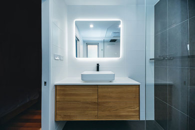 Photo of a modern bathroom in Sydney with medium wood cabinets, an open shower, multi-coloured tile, an open shower, white benchtops, a niche, a single vanity and a floating vanity.