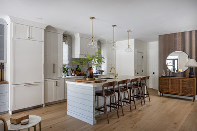 Inspiration for a 1960s galley medium tone wood floor and brown floor kitchen remodel in Philadelphia with an undermount sink, shaker cabinets, white cabinets, gray backsplash, paneled appliances, an island, white countertops and mosaic tile backsplash