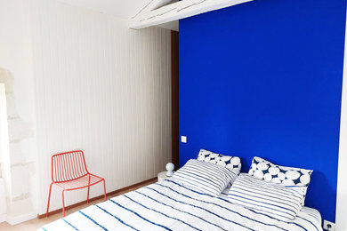 Exemple d'une petite chambre parentale tendance avec un mur bleu, parquet clair et poutres apparentes.