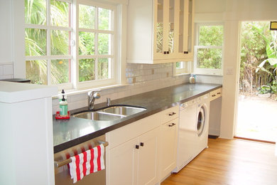Inspiration for a mid-sized galley eat-in kitchen in Santa Barbara with a double-bowl sink, shaker cabinets, white cabinets, quartz benchtops, white splashback, subway tile splashback, stainless steel appliances, light hardwood floors, no island, brown floor and black benchtop.