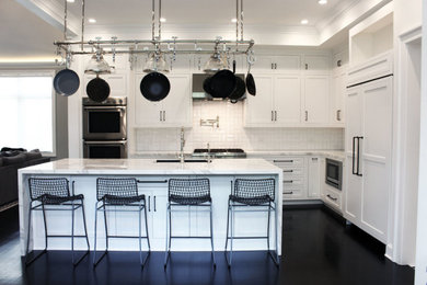 Large transitional u-shaped dark wood floor and brown floor kitchen photo in New York with an undermount sink, shaker cabinets, white cabinets, marble countertops, white backsplash, porcelain backsplash, stainless steel appliances, an island and white countertops