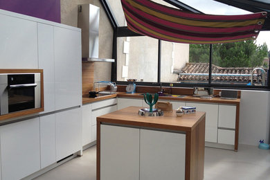 Cette image montre une cuisine design en L et inox fermée et de taille moyenne avec un évier 1 bac, un placard à porte affleurante, un plan de travail en bois, une crédence blanche, une crédence en carrelage métro, un électroménager en acier inoxydable, îlot et un sol gris.