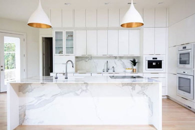 Mid-sized modern l-shaped eat-in kitchen in Raleigh with an undermount sink, flat-panel cabinets, white cabinets, quartz benchtops, white splashback, marble splashback, white appliances, medium hardwood floors, with island, brown floor and white benchtop.