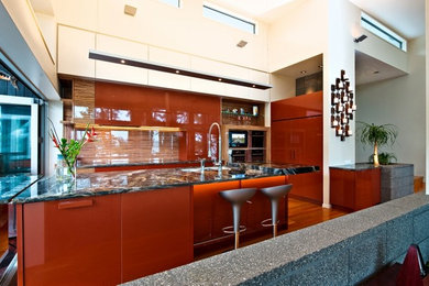 Inspiration for a large modern l-shaped eat-in kitchen in Auckland with multi-coloured splashback, glass sheet splashback, black appliances, with island, an undermount sink, flat-panel cabinets, red cabinets, granite benchtops and light hardwood floors.