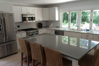 Example of a mid-sized transitional l-shaped light wood floor eat-in kitchen design in Boston with recessed-panel cabinets, white cabinets, stainless steel appliances, an island, an undermount sink and solid surface countertops