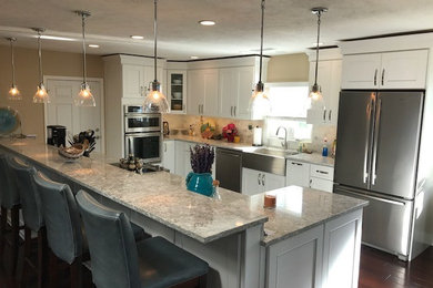 Design ideas for a mid-sized modern l-shaped eat-in kitchen in Tampa with a farmhouse sink, white cabinets, quartz benchtops, stainless steel appliances, with island, recessed-panel cabinets, beige splashback, ceramic splashback, dark hardwood floors and brown floor.